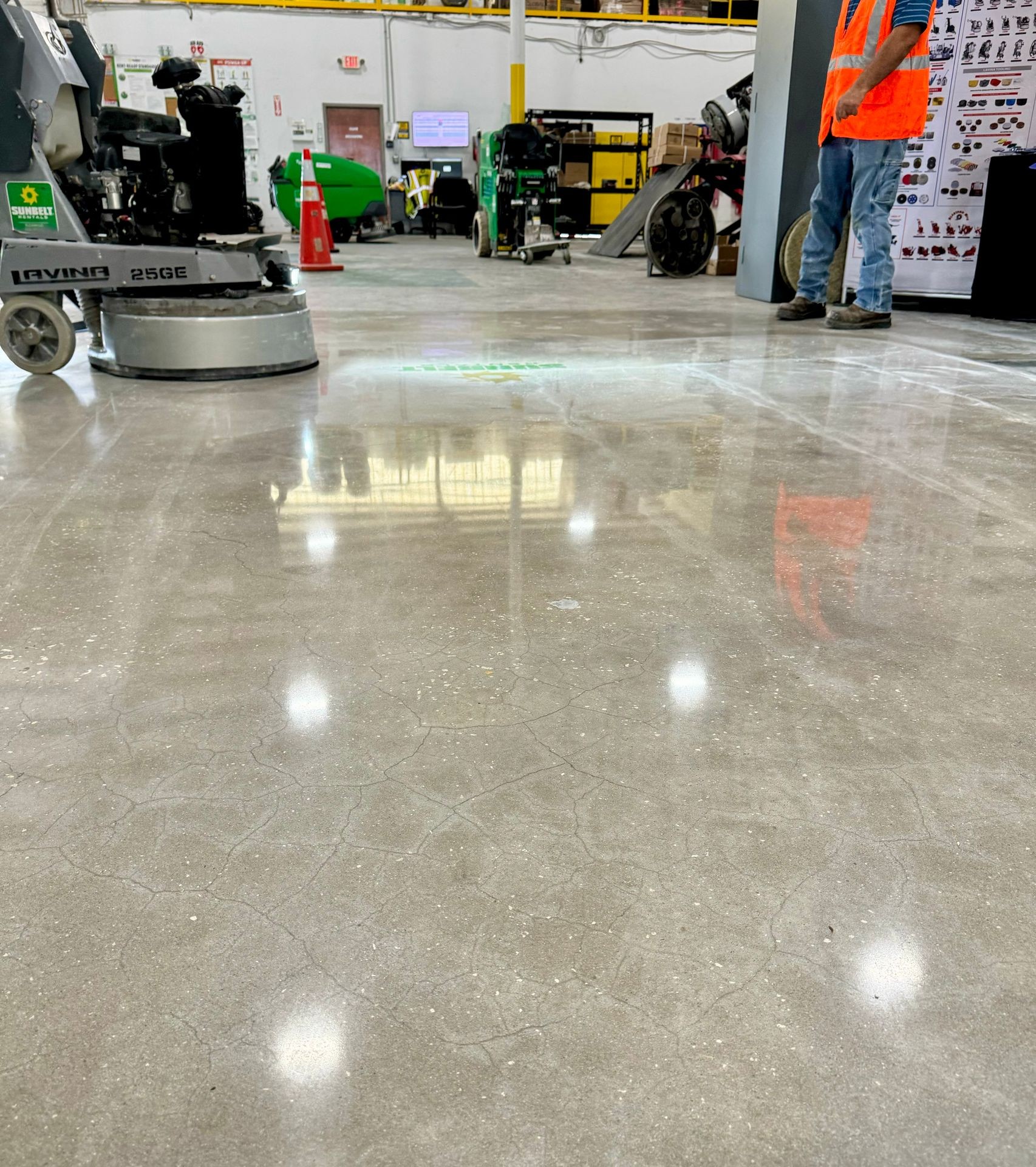 Polished concrete floor in an industrial setting with machinery and a worker wearing an orange safety vest.